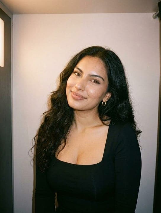 Young woman with dark wavy hair smiling gently in a photobooth