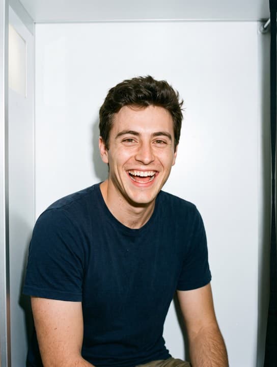 A smiling young man in his mid-twenties wearing a navy t-shirt in a photobooth